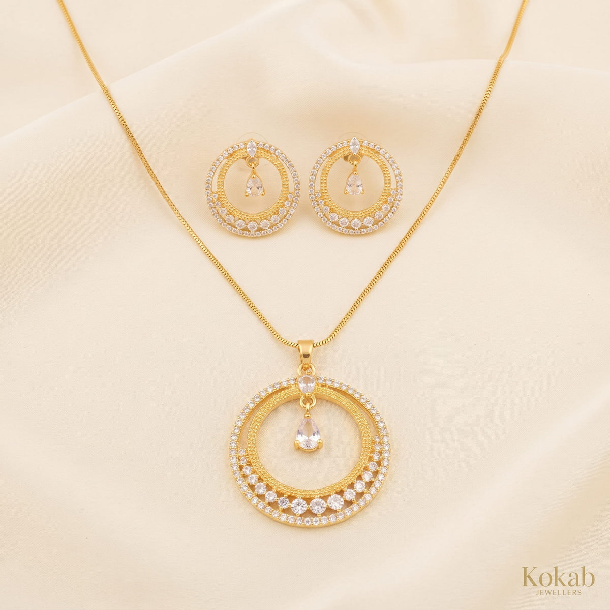 Close up of gold-plated concentric rings jewelry set featuring clear crystal stones and a suspended teardrop zircon center