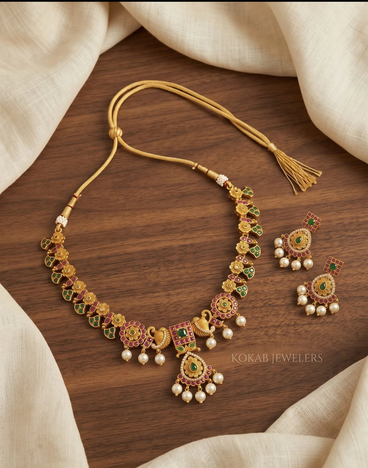 Floral gold necklace with ruby emerald stones and pearl drops on wood