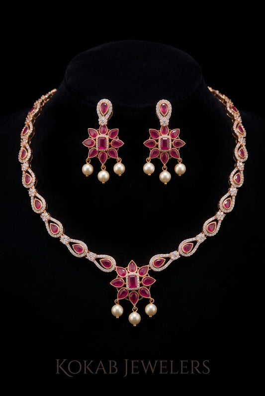 A traditional Indian jewelry set featuring a necklace and matching earrings with pink gemstones, white pearl-like drops, and gold-toned settings, displayed on a black velvet stand against a black background. The brand name 'KOKAB JEWELERS' is visible at the bottom.