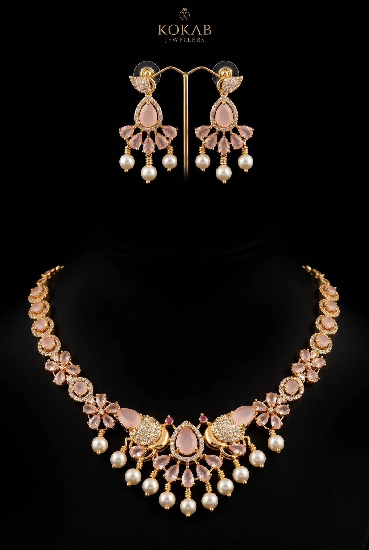A gold-plated jewelry set by Kokab Jewellers, featuring a statement necklace and matching drop earrings. The set is embellished with light pink stones, clear crystals, and white faux pearls, displayed on a black background.