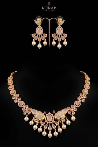 A gold-plated jewelry set by Kokab Jewellers, featuring a statement necklace and matching drop earrings. The set is embellished with light pink stones, clear crystals, and white faux pearls, displayed on a black background.